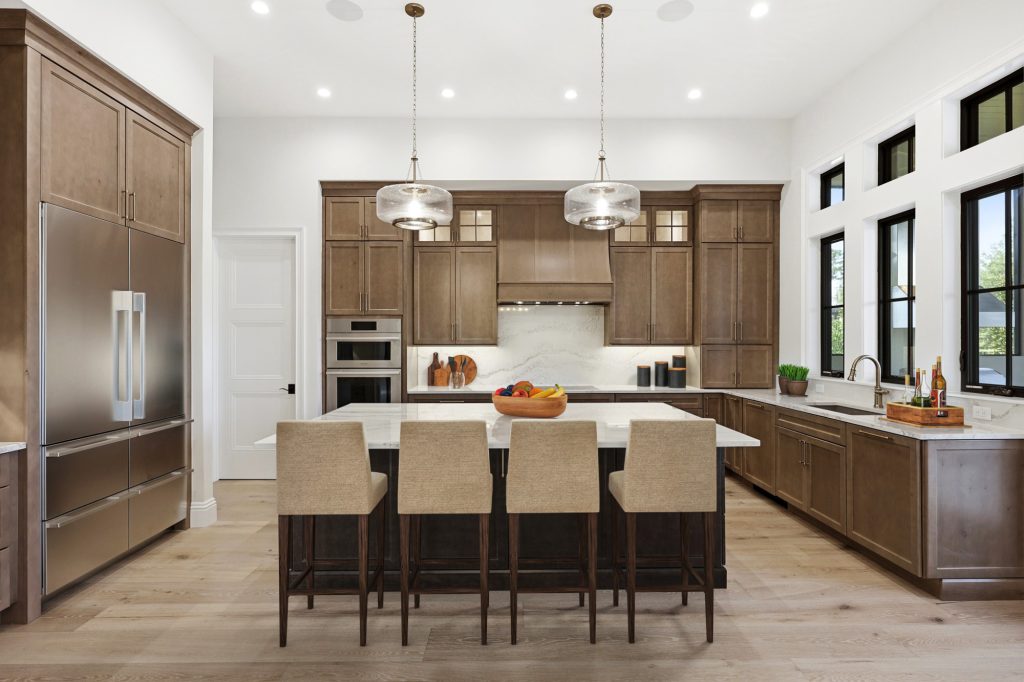 Kitchen with stained wood cabinetry, a large white-topped island with four upholstered barstools, and two glass pendant lights.